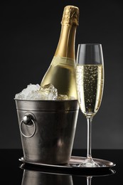 Photo of Glass of sparkling wine and bottle in cooler bucket on black mirror surface