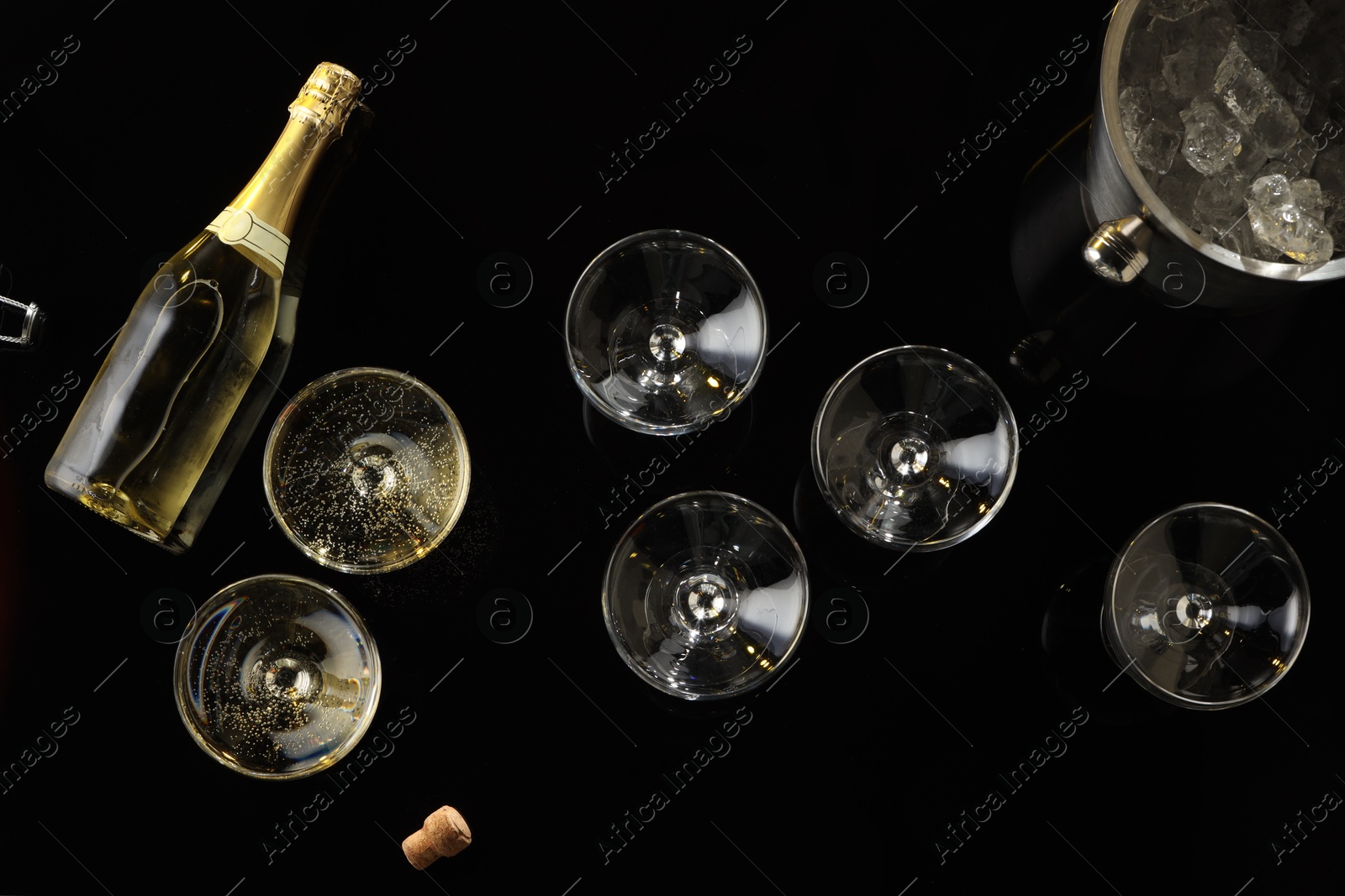 Photo of Bottle of sparkling wine, glasses and cooler bucket on black table, flat lay