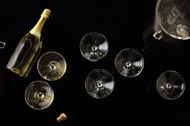 Photo of Bottle of sparkling wine, glasses and cooler bucket on black table, flat lay