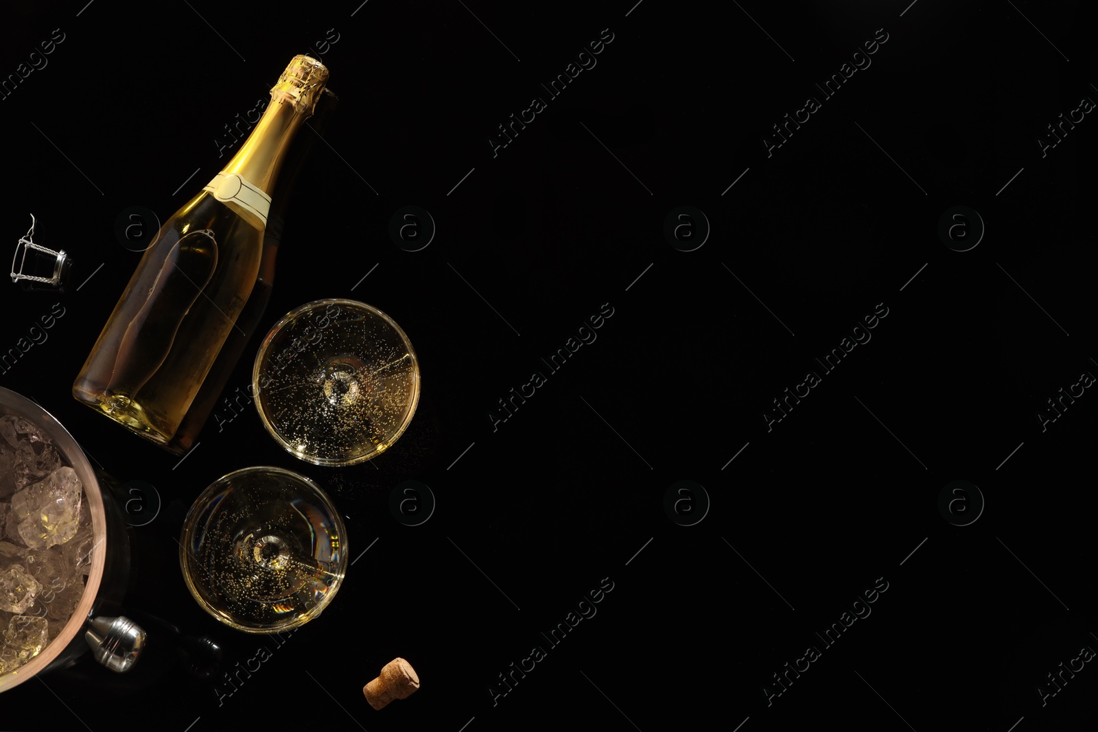 Photo of Bottle of sparkling wine, glasses and cooler bucket on black table, flat lay. Space for text