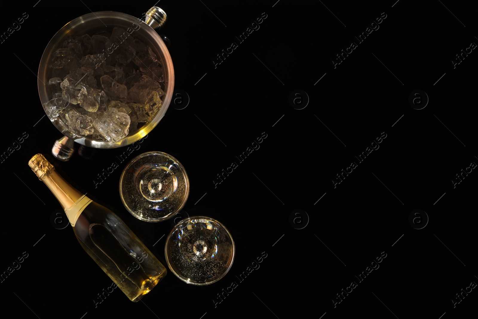 Photo of Bottle of sparkling wine, glasses and cooler bucket on black table, flat lay. Space for text