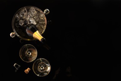 Photo of Bottle of sparkling wine in cooler bucket and glasses on black table, flat lay. Space for text