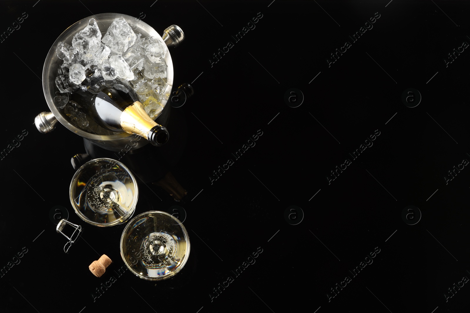 Photo of Bottle of sparkling wine in cooler bucket and glasses on black table, flat lay. Space for text