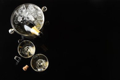 Photo of Bottle of sparkling wine in cooler bucket and glasses on black table, flat lay. Space for text