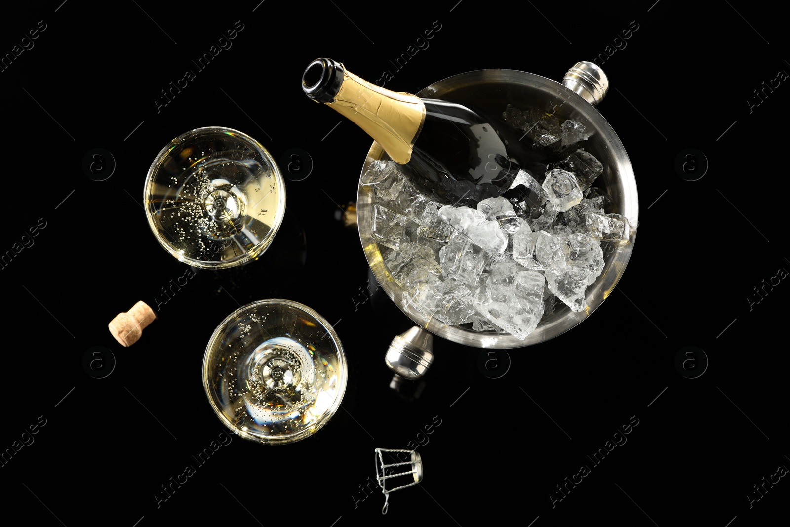 Photo of Bottle of sparkling wine in cooler bucket and glasses on black table, flat lay