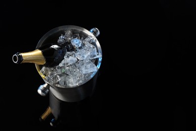 Photo of Bottle of sparkling wine in cooler bucket on black mirror surface, above view. Space for text