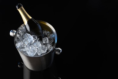 Photo of Bottle of sparkling wine in cooler bucket on black mirror surface, above view. Space for text