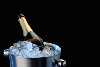 Photo of Bottle of sparkling wine in cooler bucket on black background, closeup. Space for text