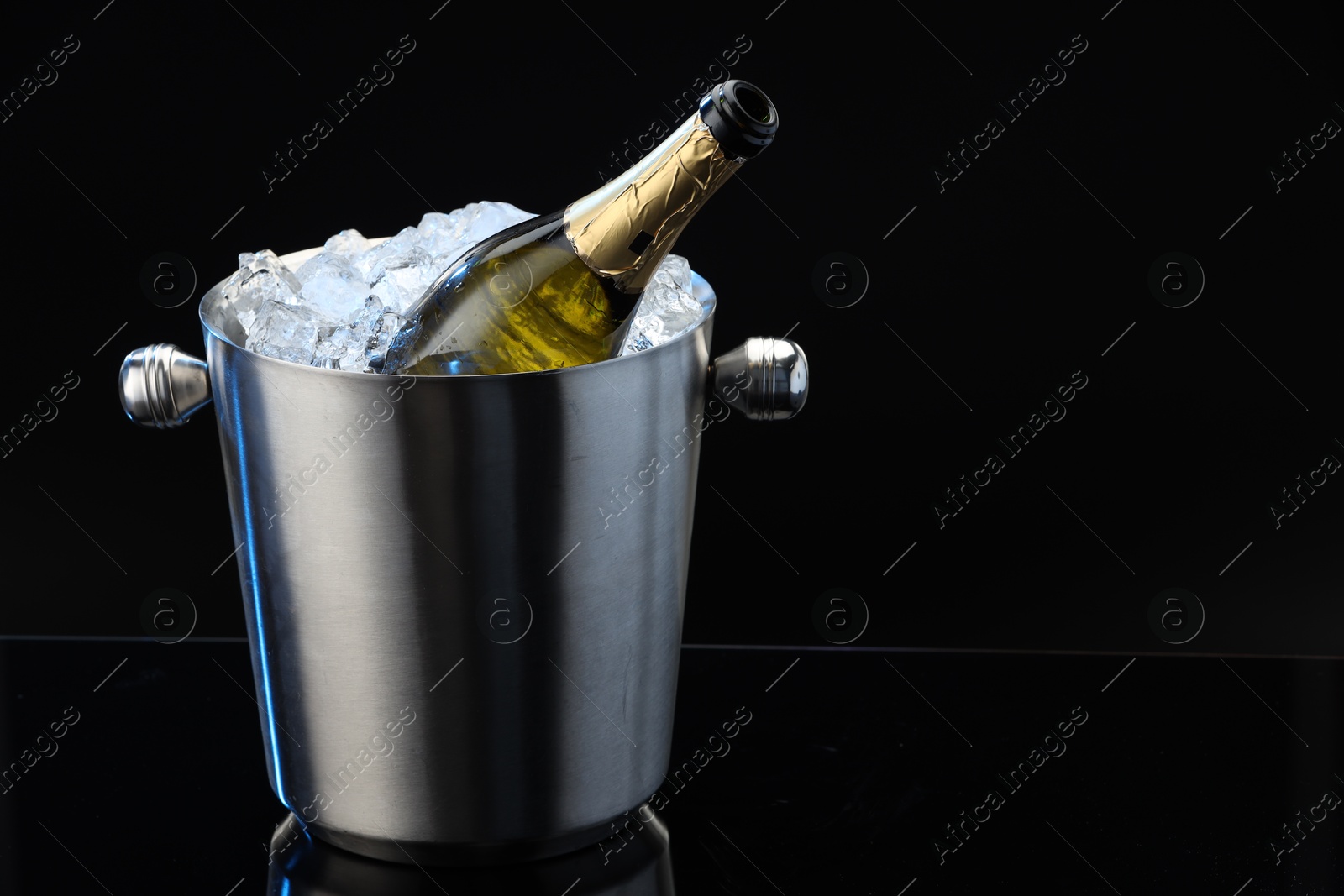 Photo of Bottle of sparkling wine in cooler bucket on black mirror surface. Space for text