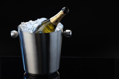 Bottle of sparkling wine in cooler bucket on black mirror surface. Space for text