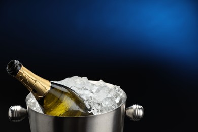 Photo of Bottle of sparkling wine in cooler bucket on blue background, closeup. Space for text