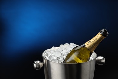 Photo of Bottle of sparkling wine in cooler bucket on blue background, closeup. Space for text