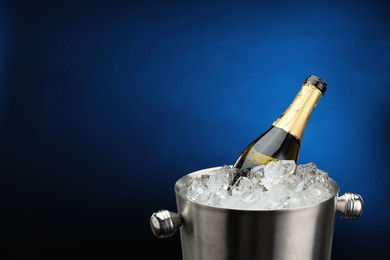 Photo of Bottle of sparkling wine in cooler bucket on blue background, closeup. Space for text