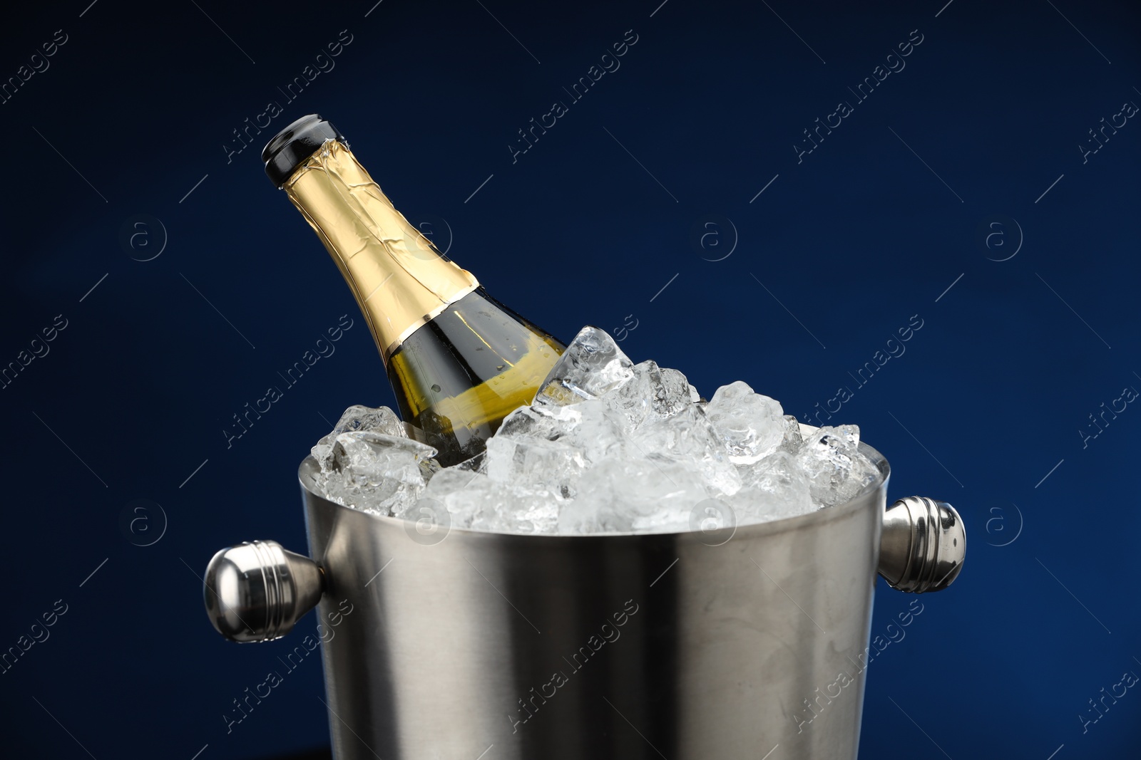 Photo of Bottle of sparkling wine in cooler bucket on blue background, closeup