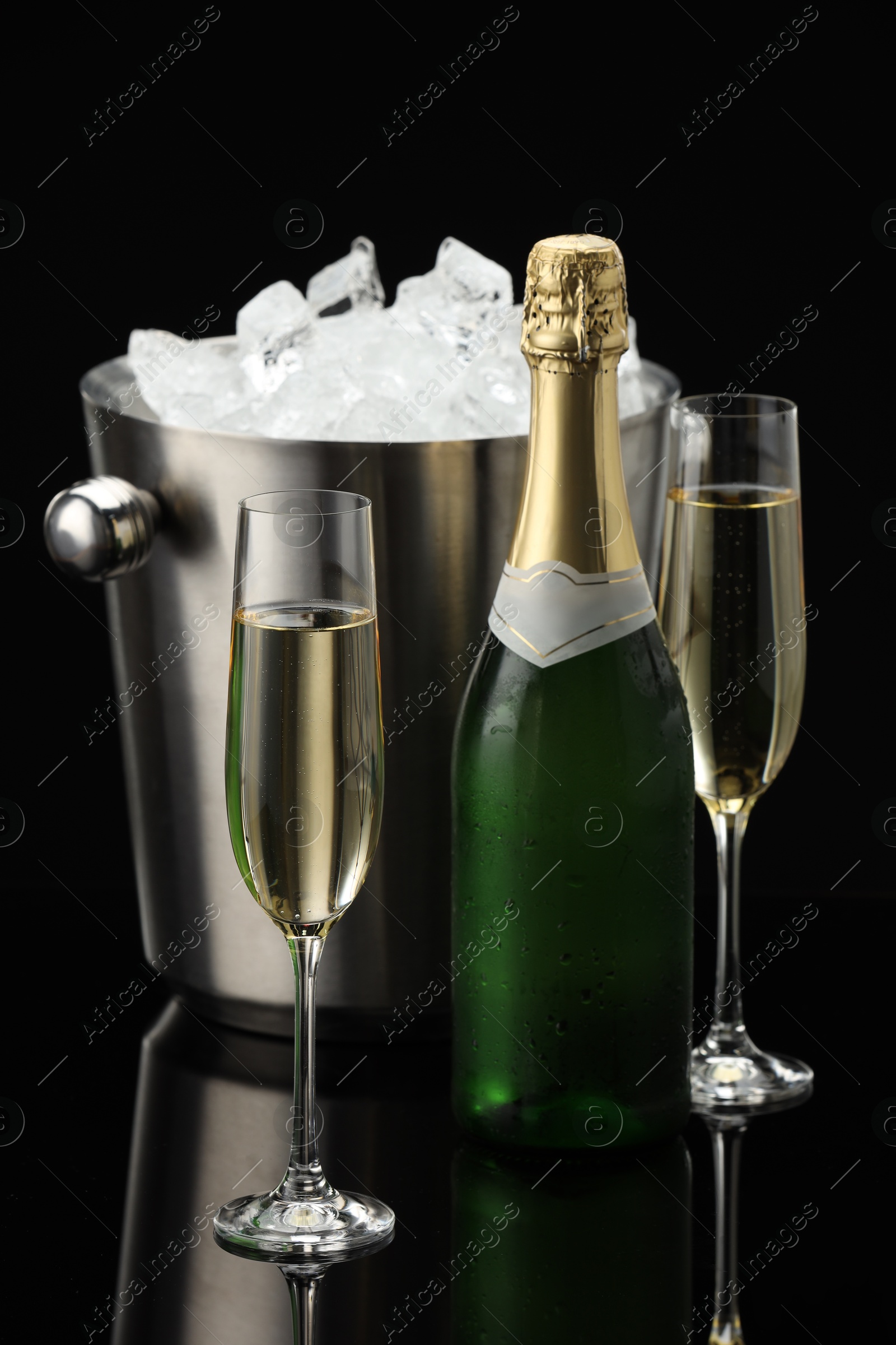 Photo of Bottle of sparkling wine, glasses and cooler bucket on black mirror surface