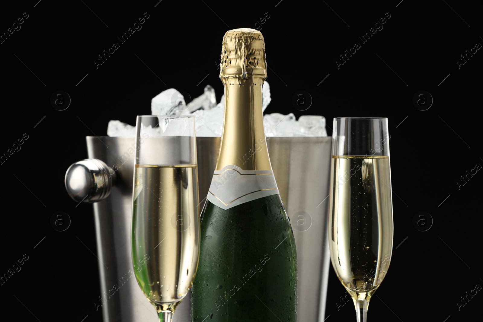 Photo of Bottle of sparkling wine, glasses and cooler bucket on black background, closeup