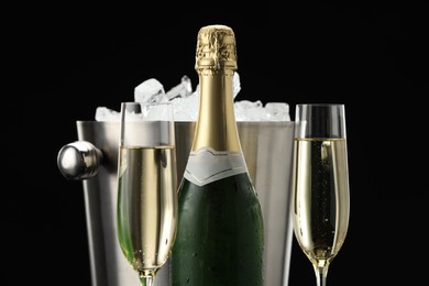 Photo of Bottle of sparkling wine, glasses and cooler bucket on black background, closeup