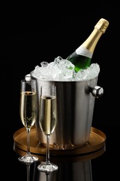 Photo of Bottle of sparkling wine in cooler bucket and glasses against black background