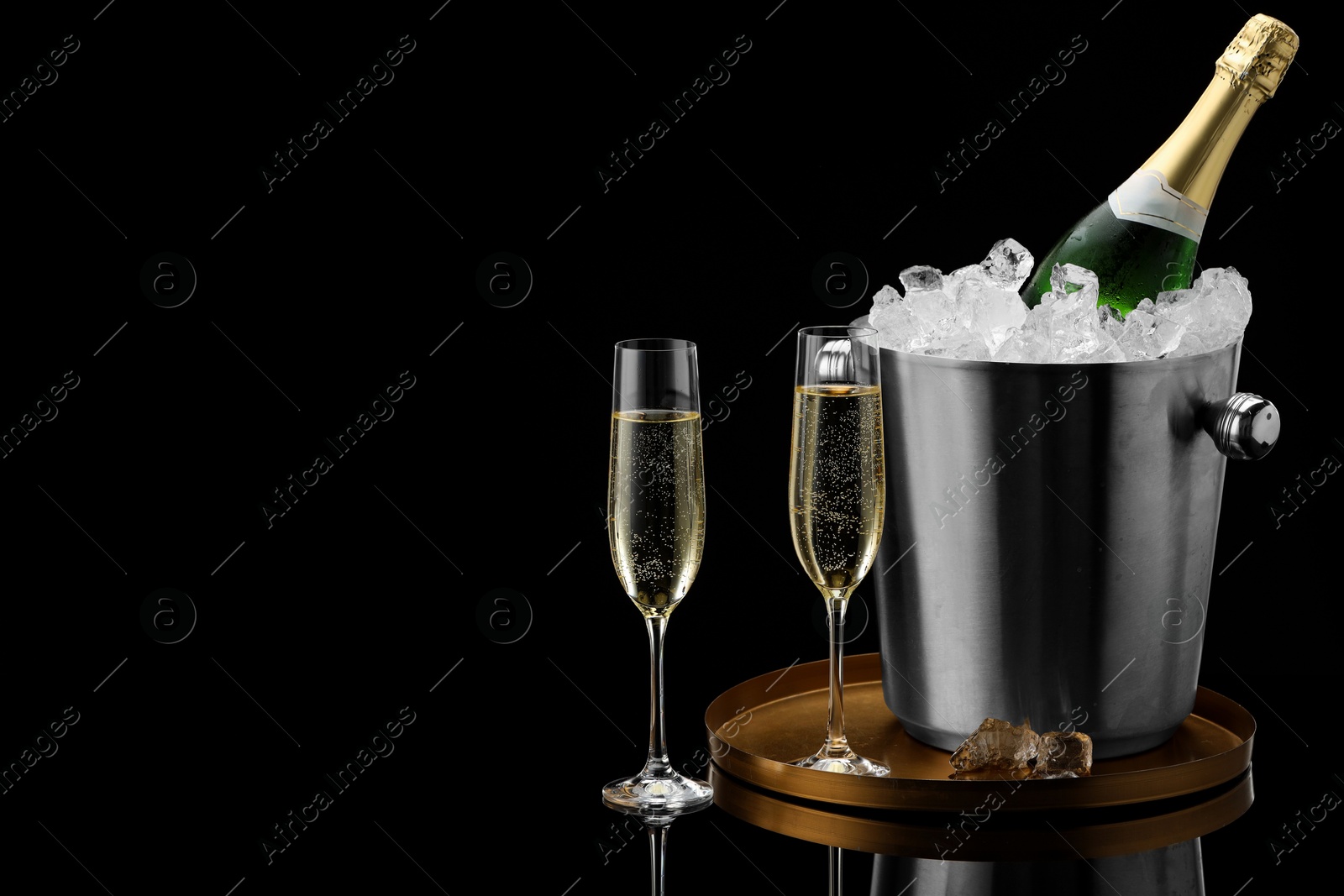 Photo of Bottle of sparkling wine in cooler bucket and glasses against black background. Space for text