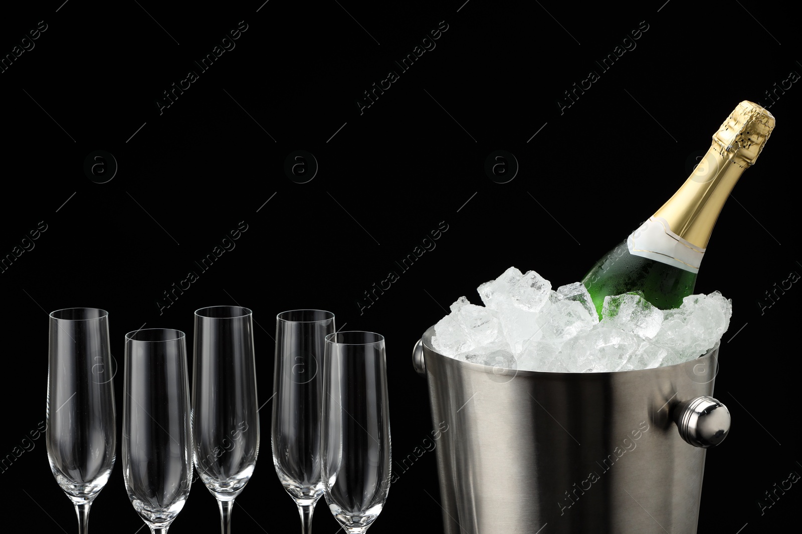 Photo of Bottle of sparkling wine in cooler bucket and glasses against black background, closeup. Space for text