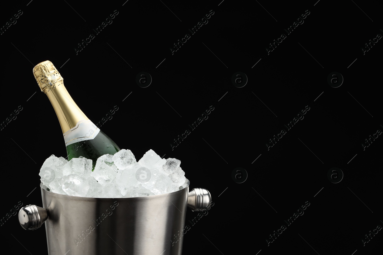 Photo of Bottle of sparkling wine in cooler bucket against black background, closeup. Space for text