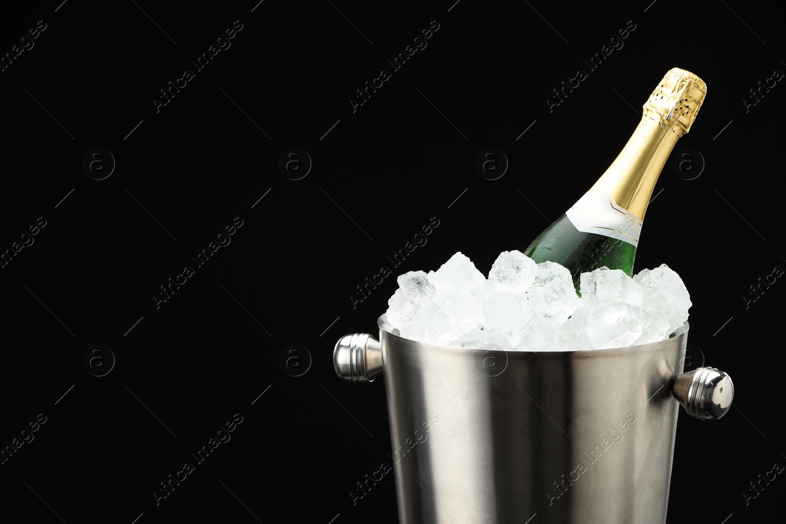 Photo of Bottle of sparkling wine in cooler bucket on black background, closeup. Space for text