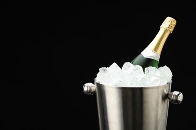 Photo of Bottle of sparkling wine in cooler bucket on black background, closeup. Space for text