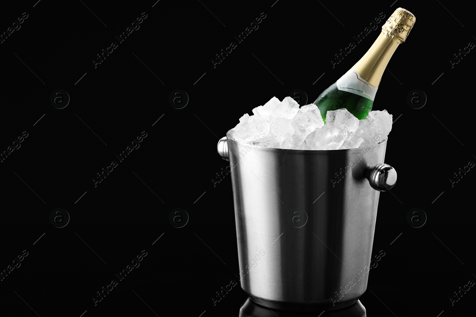 Photo of Bottle of sparkling wine in cooler bucket on black mirror surface. Space for text