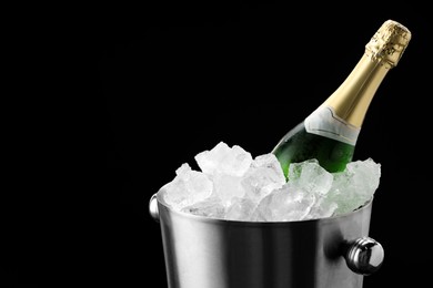 Photo of Bottle of sparkling wine in cooler bucket on black background, closeup. Space for text