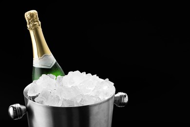 Photo of Bottle of sparkling wine in cooler bucket on black background, closeup. Space for text