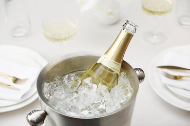 Bottle of sparkling wine in cooler bucket and glasses on light table, closeup