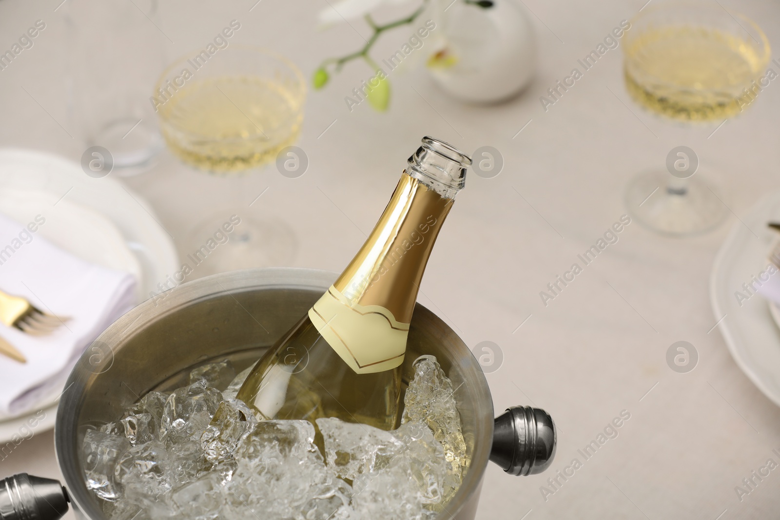 Photo of Bottle of sparkling wine in cooler bucket and glasses on light table, closeup