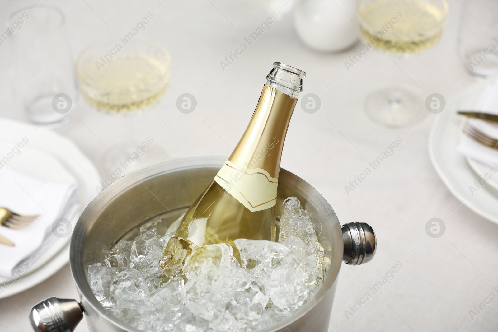 Photo of Bottle of sparkling wine in cooler bucket and glasses on light table, closeup