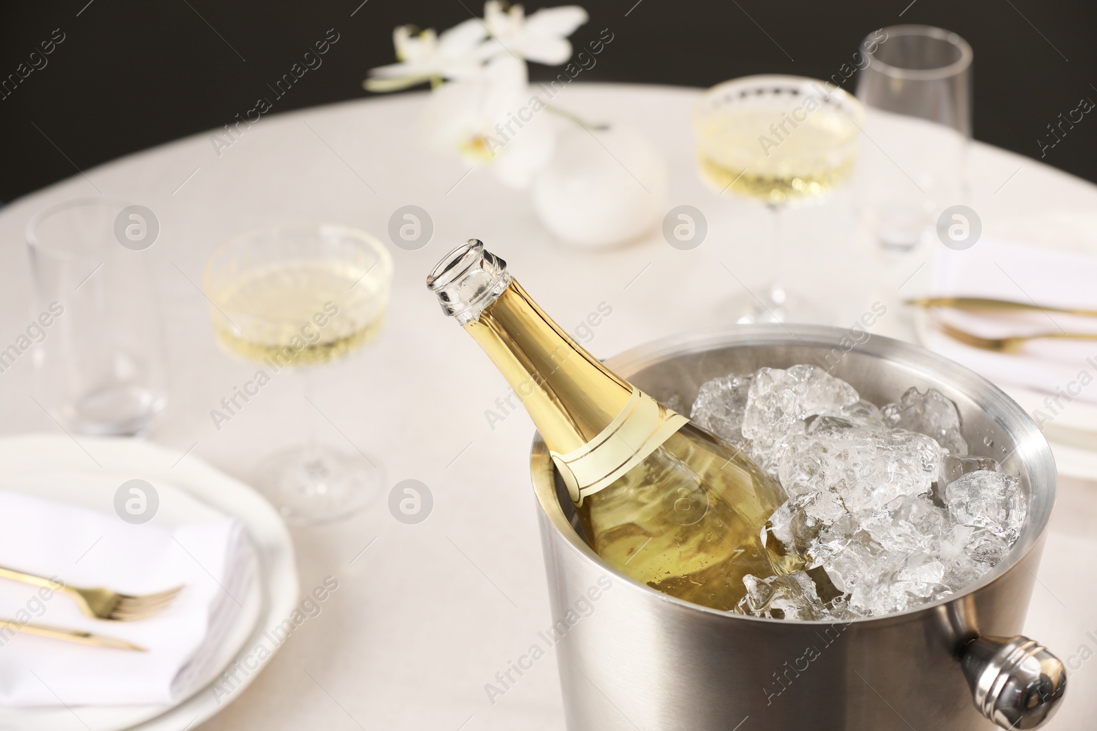 Photo of Bottle of sparkling wine in cooler bucket and glasses on light table, closeup