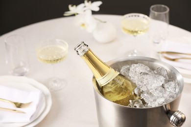 Bottle of sparkling wine in cooler bucket and glasses on light table, closeup