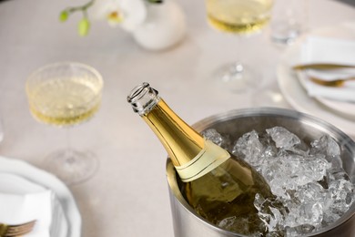 Photo of Bottle of sparkling wine in cooler bucket and glasses on light table, closeup