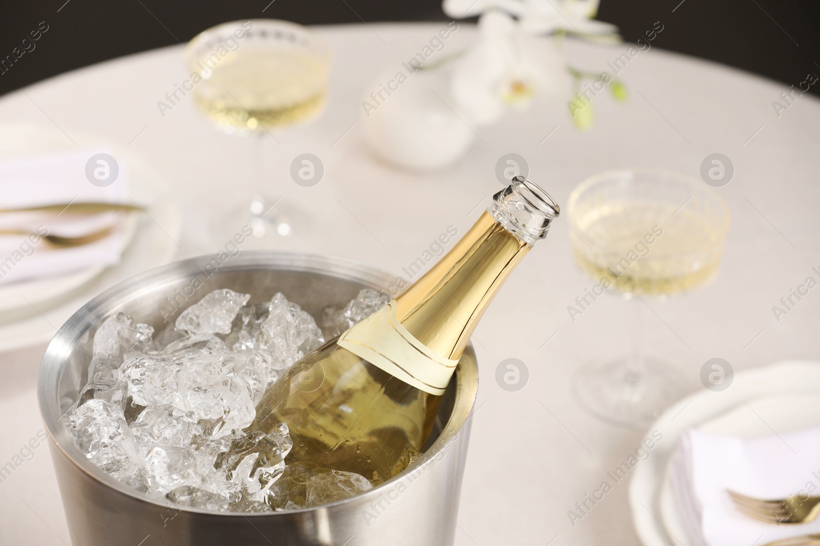 Photo of Bottle of sparkling wine in cooler bucket and glasses on light table, closeup