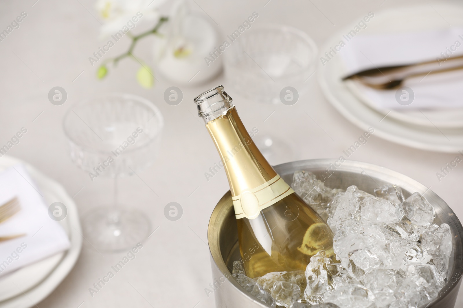 Photo of Bottle of sparkling wine in cooler bucket and glasses on light table, closeup