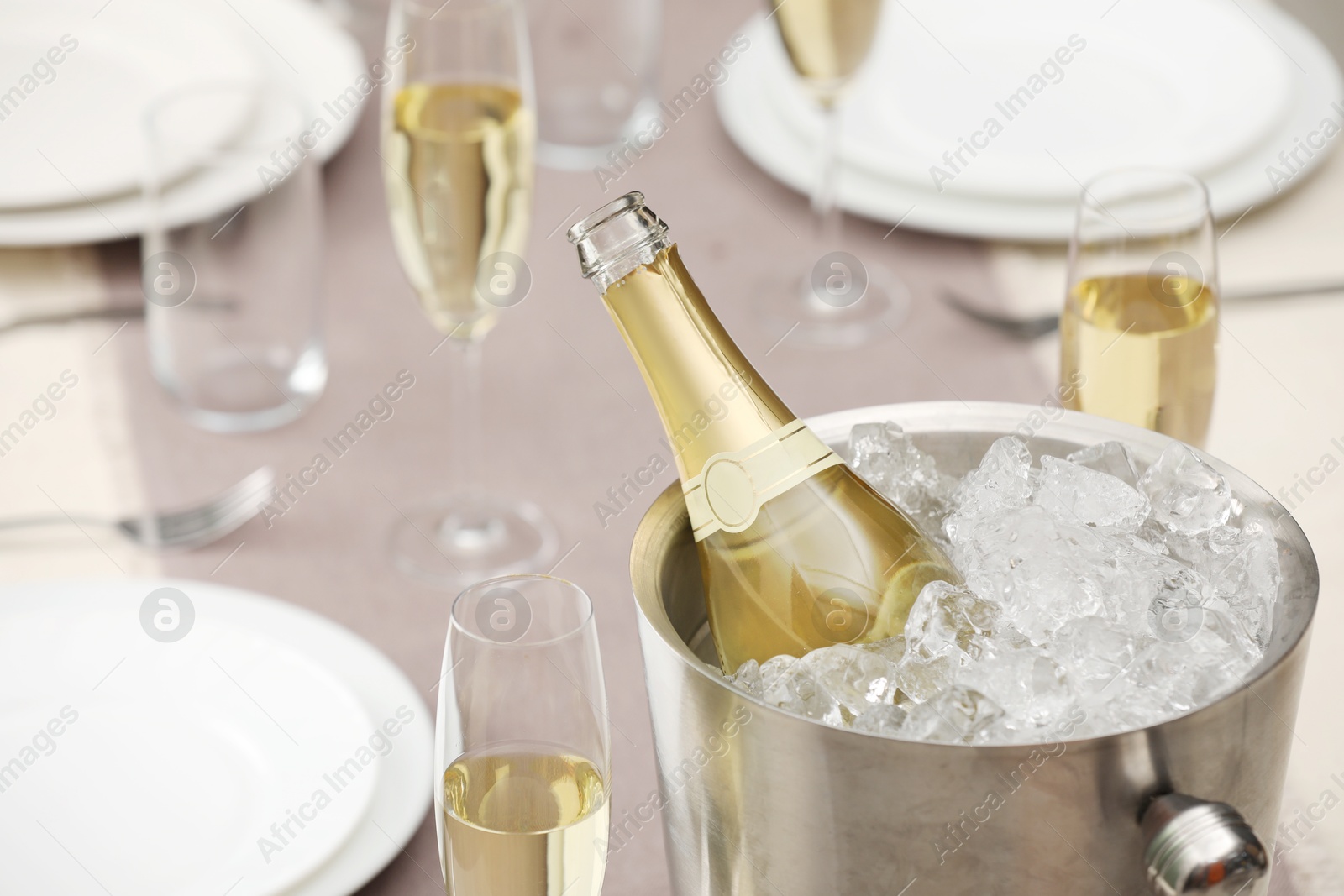 Photo of Bottle of sparkling wine in cooler bucket and glasses on light table, closeup