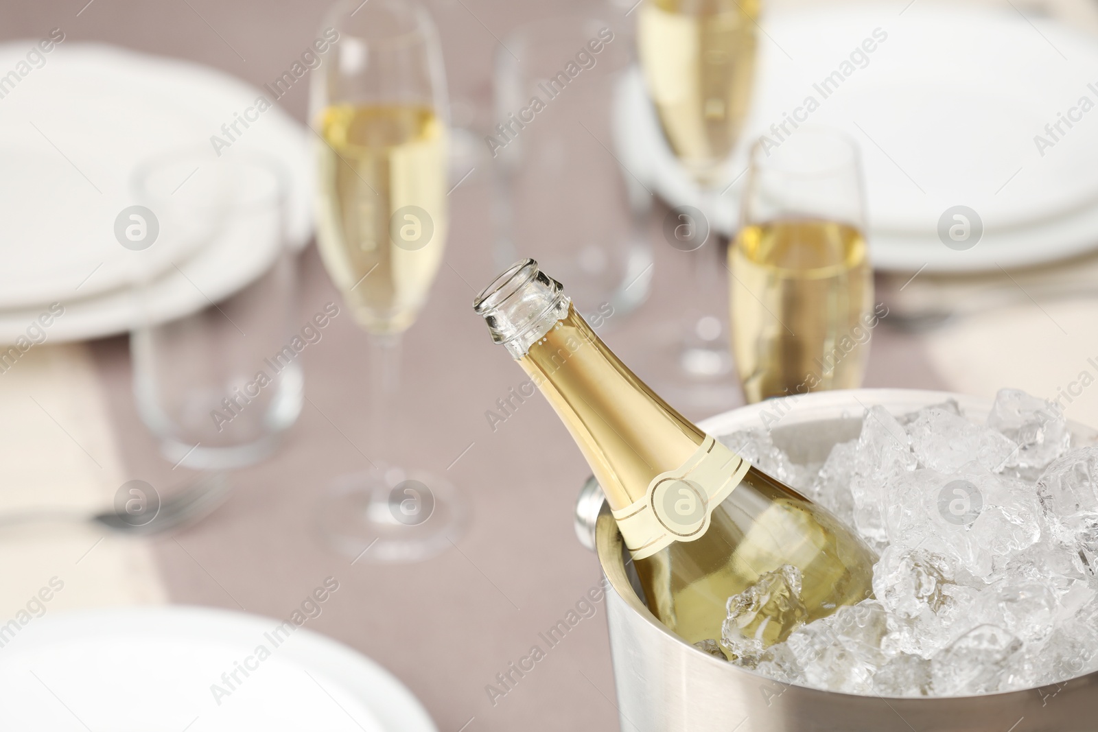 Photo of Bottle of sparkling wine in cooler bucket and glasses on light table, closeup