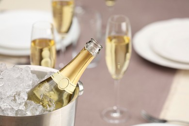 Photo of Bottle of sparkling wine in cooler bucket and glasses on light table, closeup