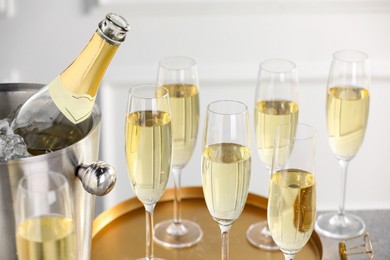 Photo of Bottle of sparkling wine in cooler bucket and glasses on table, closeup