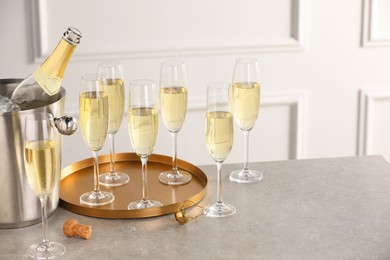 Photo of Bottle of sparkling wine in cooler bucket and glasses on grey table