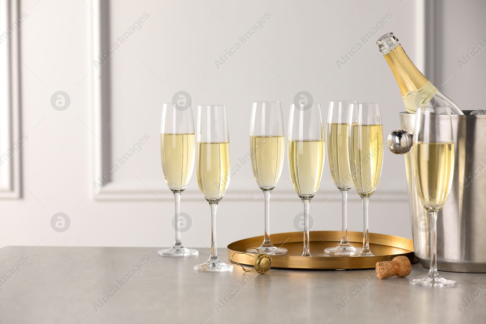 Photo of Bottle of sparkling wine in cooler bucket and glasses on grey table