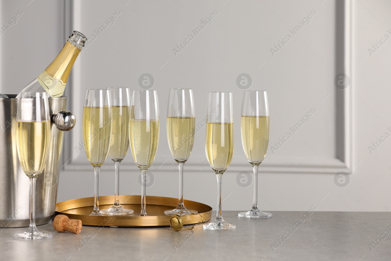 Photo of Bottle of sparkling wine in cooler bucket and glasses on grey table