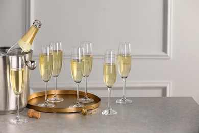 Photo of Bottle of sparkling wine in cooler bucket and glasses on grey table