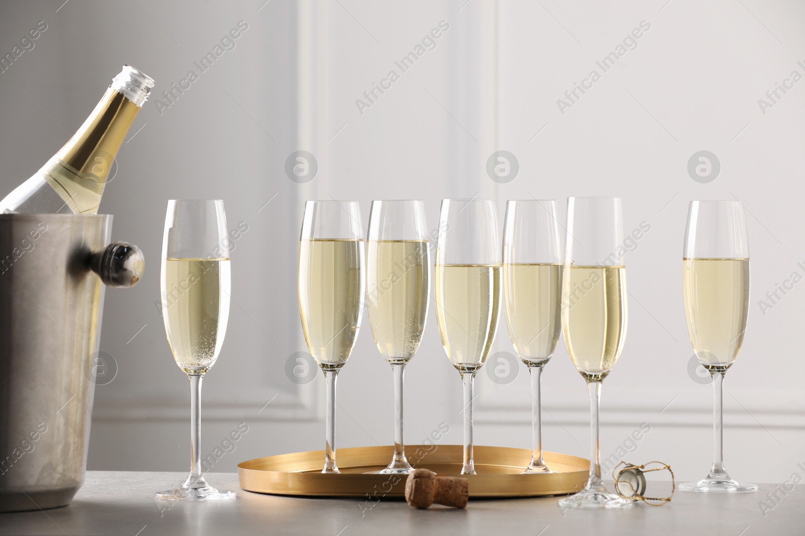 Photo of Bottle of sparkling wine in cooler bucket and glasses on grey table