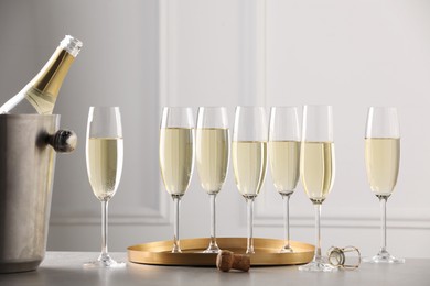 Photo of Bottle of sparkling wine in cooler bucket and glasses on grey table