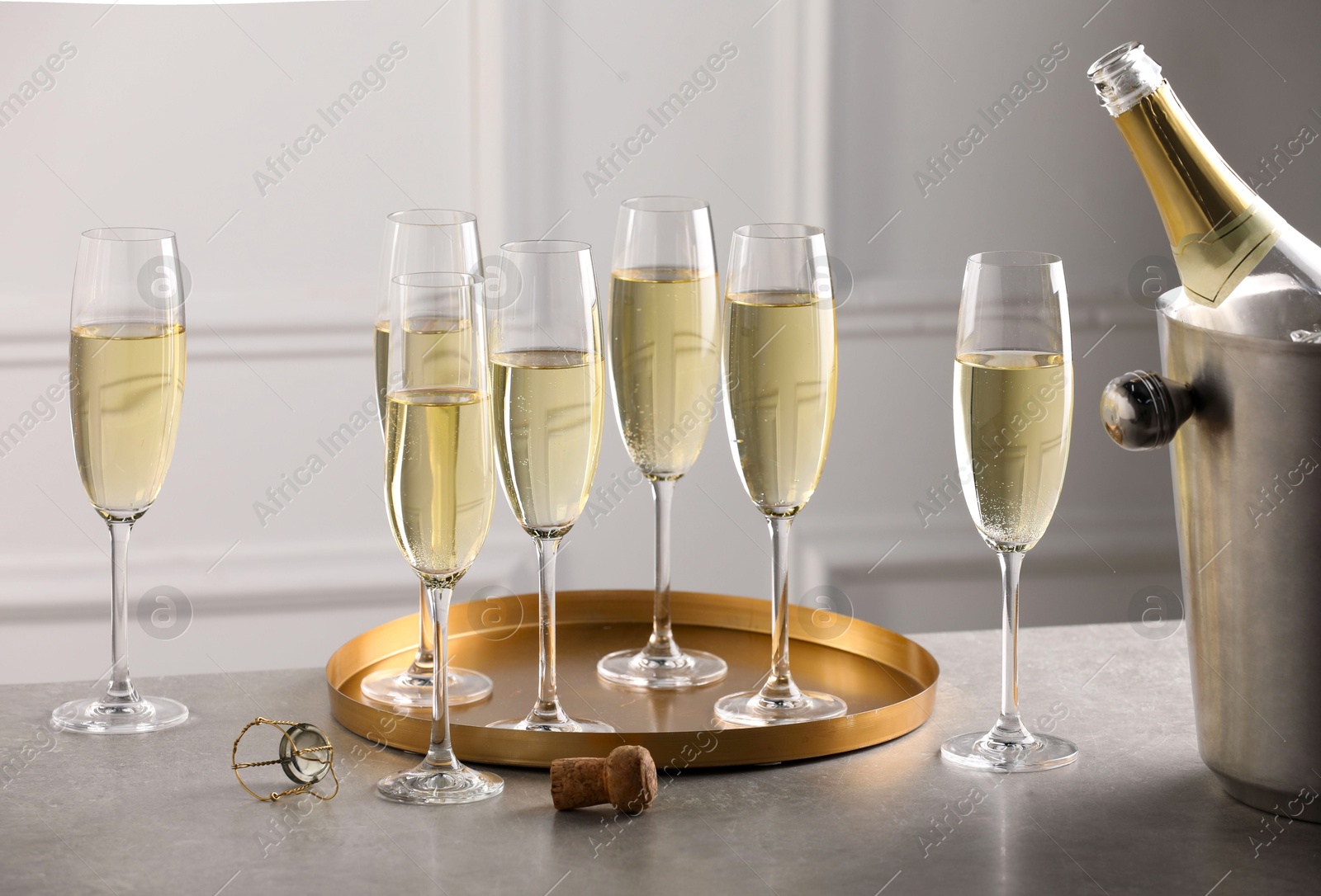 Photo of Bottle of sparkling wine in cooler bucket and glasses on grey table