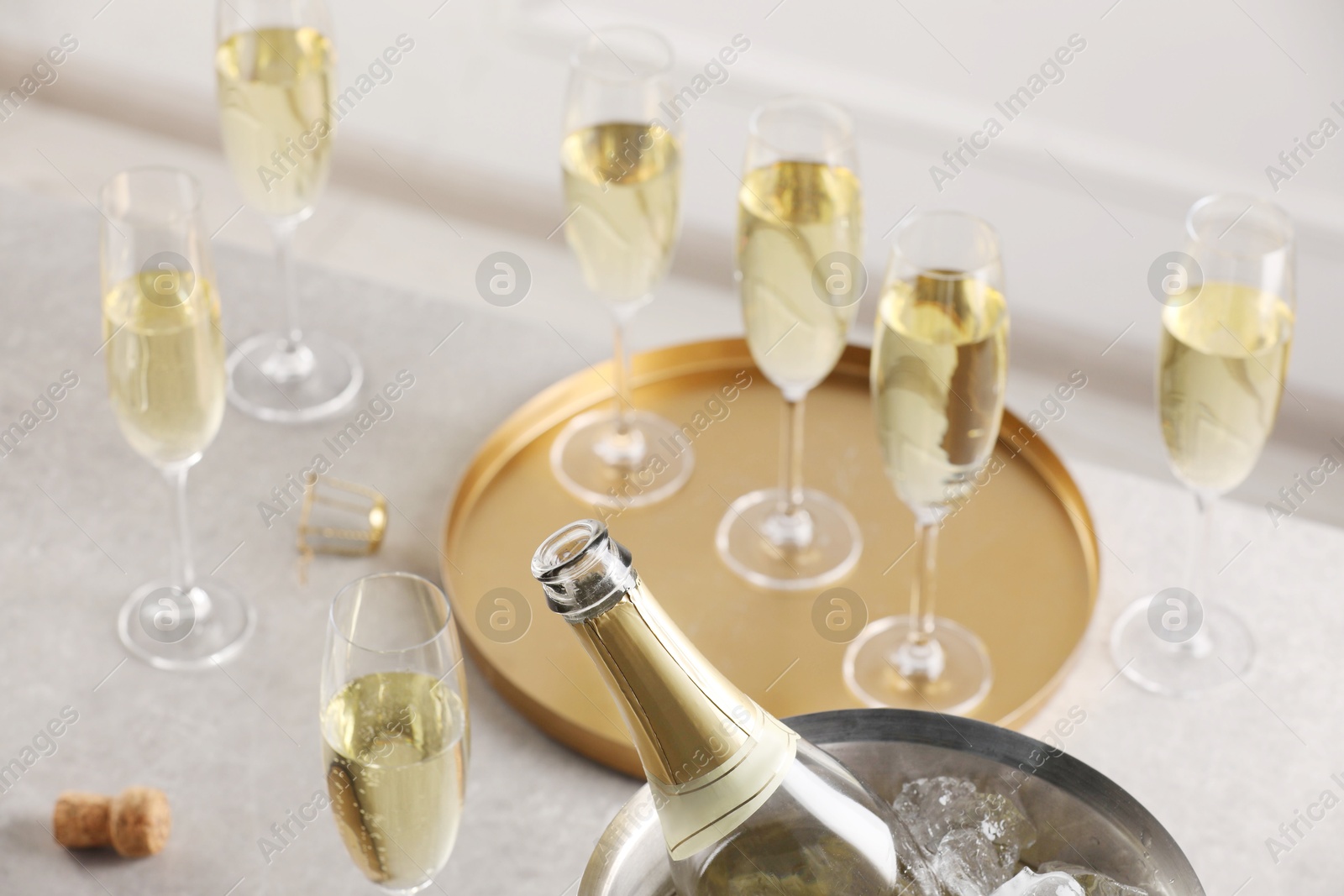 Photo of Bottle of sparkling wine in cooler bucket and glasses on light table, closeup